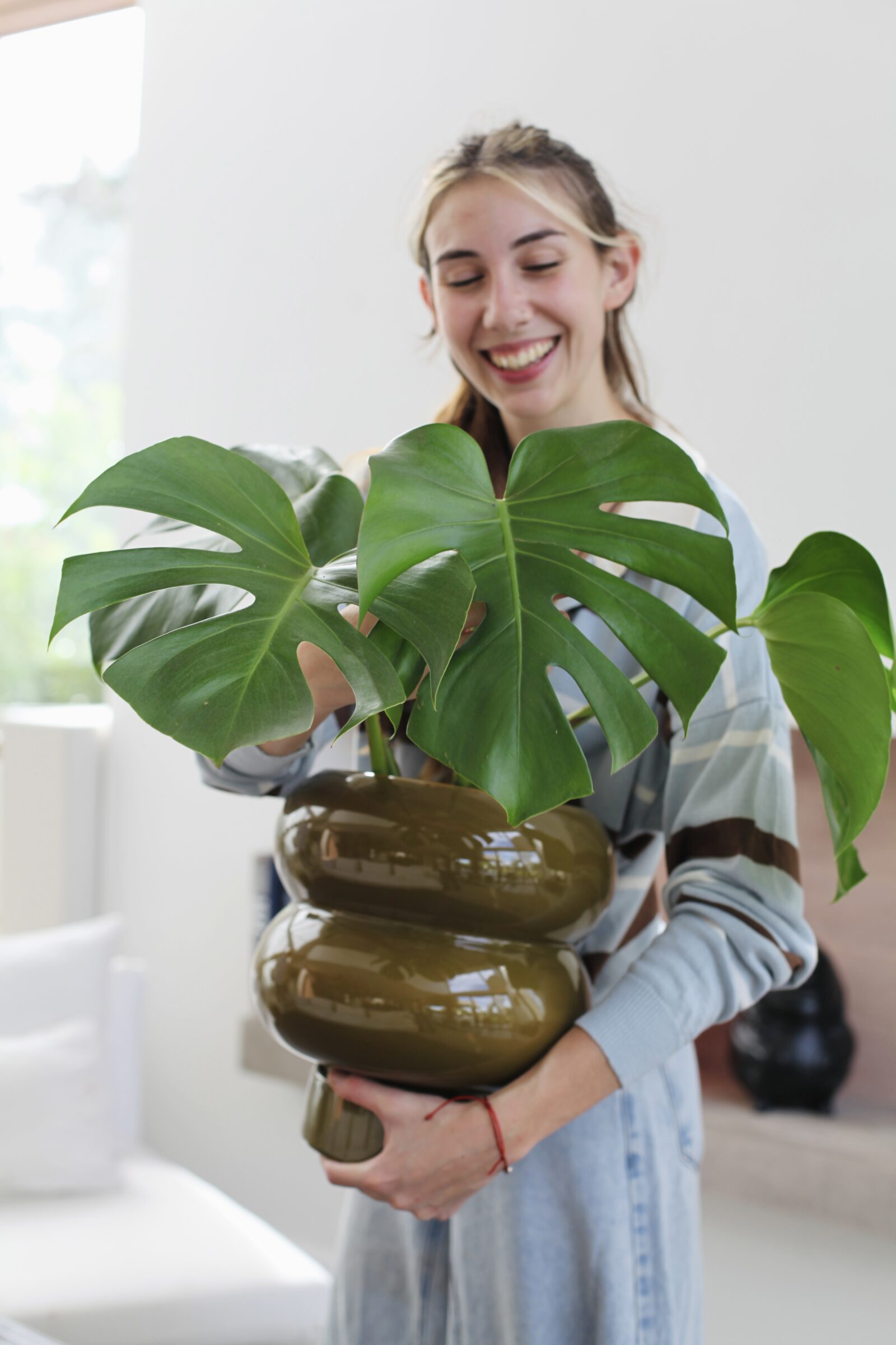 Mujer sosteniendo Monstera deliciosa sana en maceta cerámica verde oliva, guía completa de cuidados de la Monstera