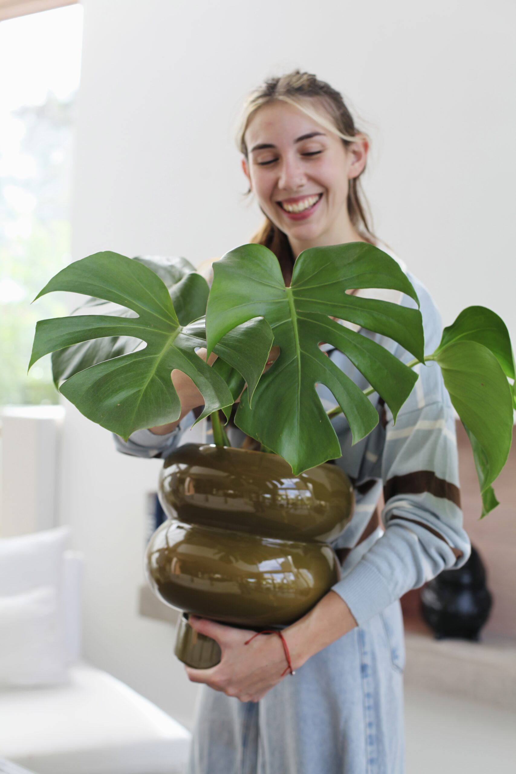 Mujer sosteniendo Monstera deliciosa sana en maceta cerámica verde oliva, guía completa de cuidados de la Monstera